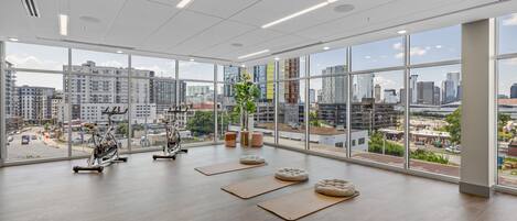 A spacious gym with large windows, exercise equipment, and a city view.