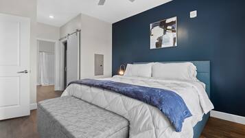 Quarto com uma cama, um banquinho, um ventilador de teto e um quadro na parede.