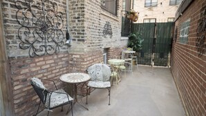A courtyard with a brick wall, metal chairs, a small round table, and a hanging flower basket.