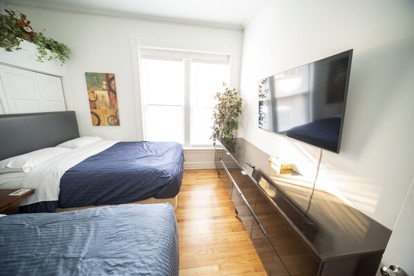A modern hotel room with two beds, a flat-screen TV, a large window, and a plant. - Extra Large Authentic Chicago Graystone walk to Wrigley, Lakefront & Restaurants (Chicago)