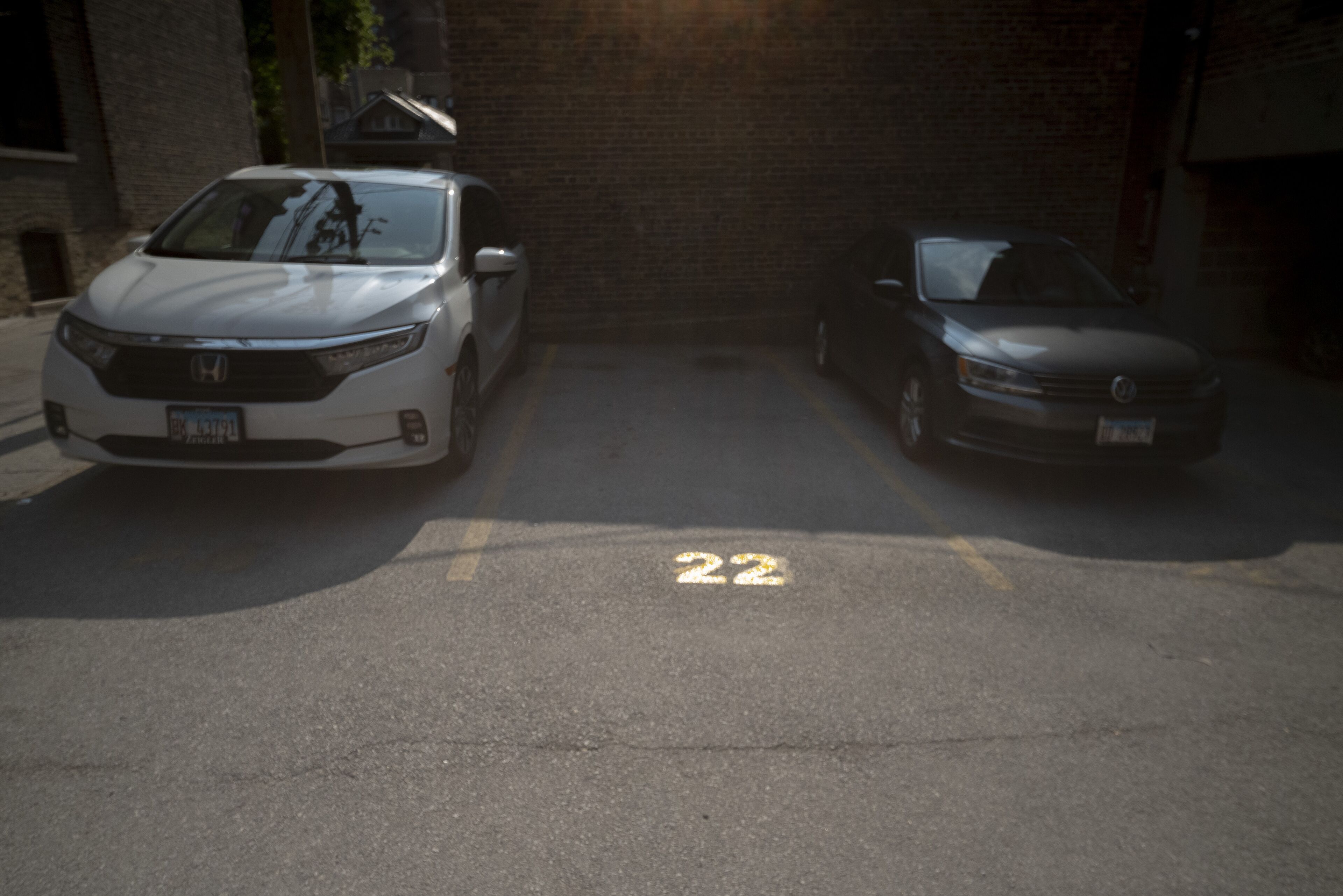 Dos coches estacionados en un estacionamiento, con un muro de ladrillo al fondo.