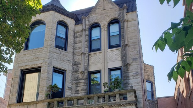 A historic stone building with a prominent entrance, large windows, and a small balcony with potted plants.
