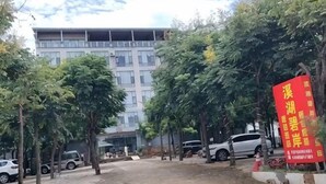 A parking area with trees and a building in the background. - Guiyuanju Hotel (Huaning)