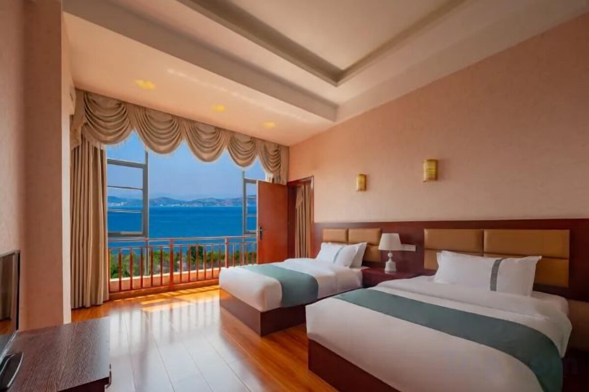 A hotel room with two beds, a view of the sea, and a balcony.