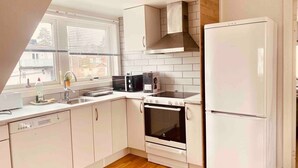 Una cucina moderna con mobili bianchi, forno integrato, microonde, lavastoviglie e frigorifero.