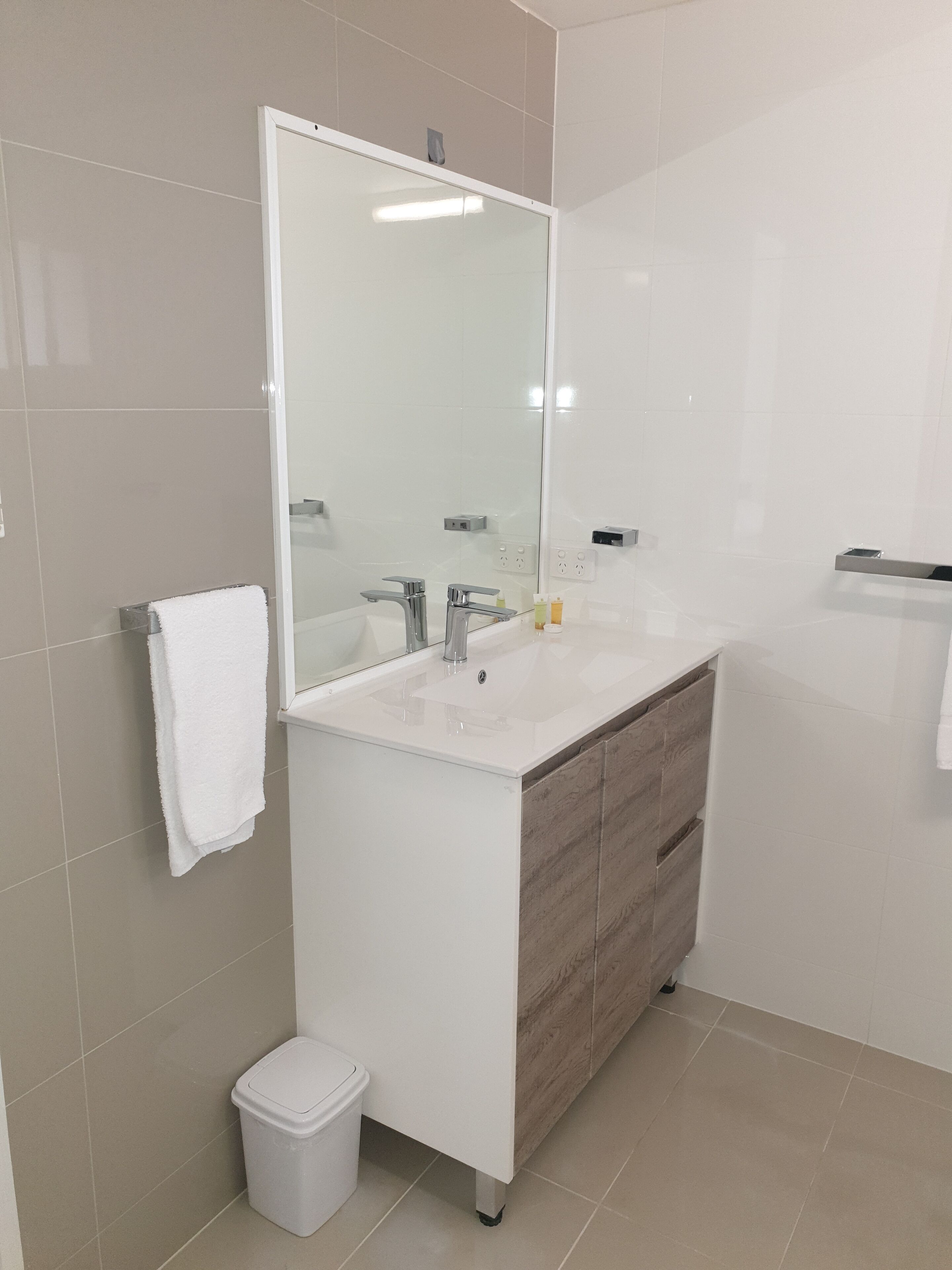 Een moderne badkamer met een wit aanrichtmeubel, een grote spiegel en een handdoek aan de muur.