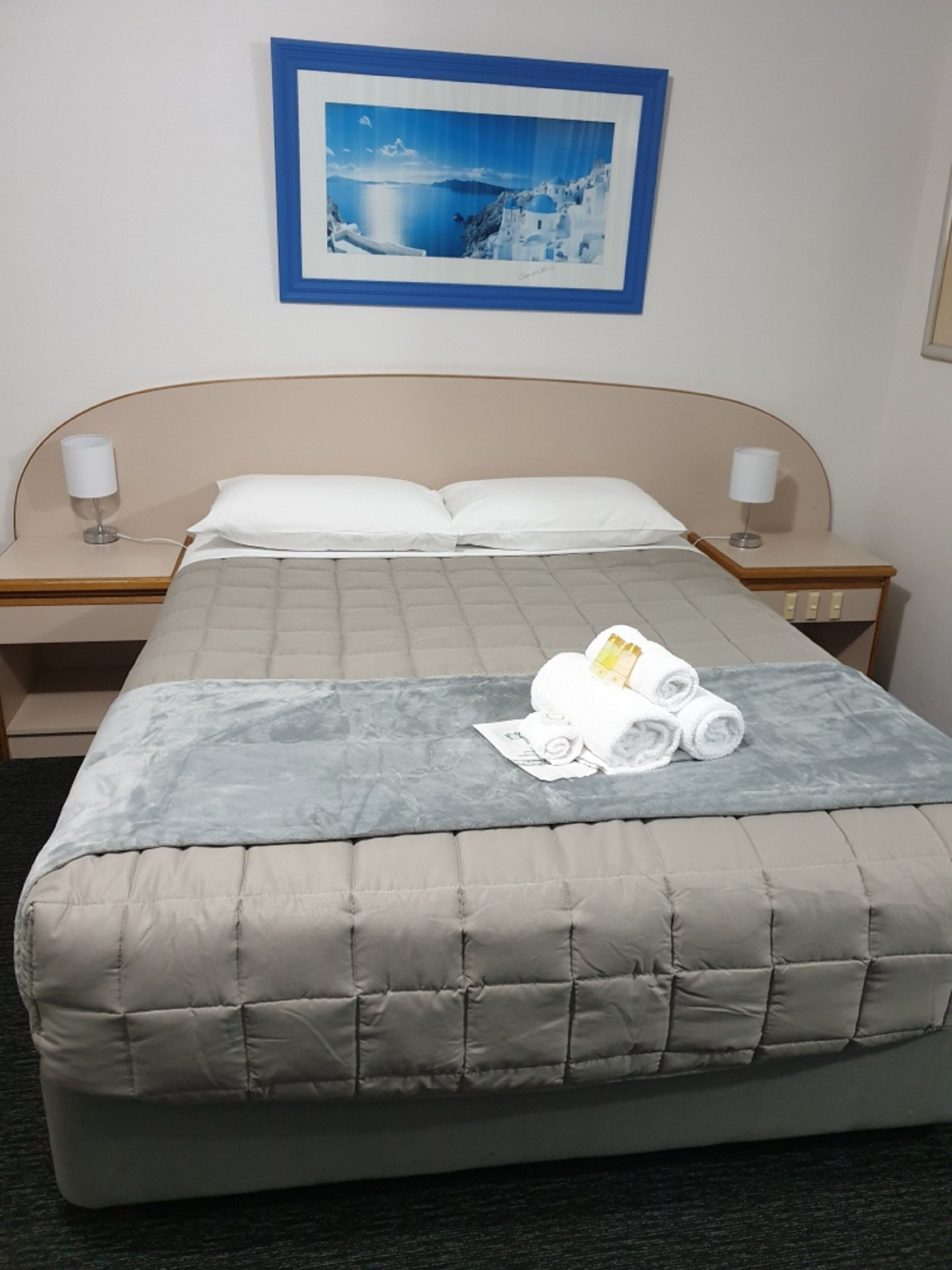 A hotel room with a bed, two bedside tables, a framed picture on the wall, and a towel on the bed.