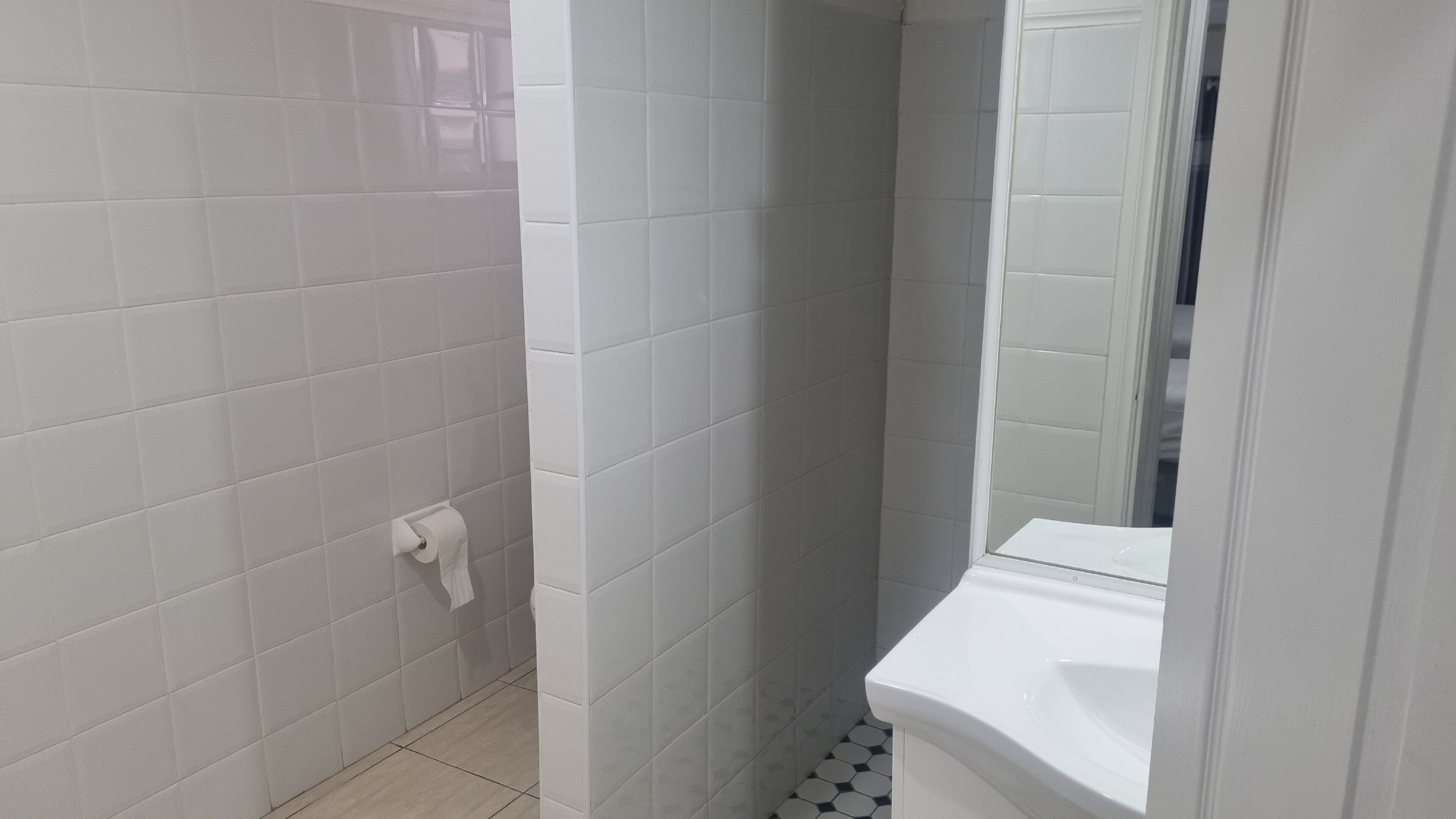 A bathroom with white tiled walls and a white toilet.