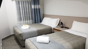 Habitación de hotel con dos camas, una mesita de noche, una lámpara y una ventana con cortinas.