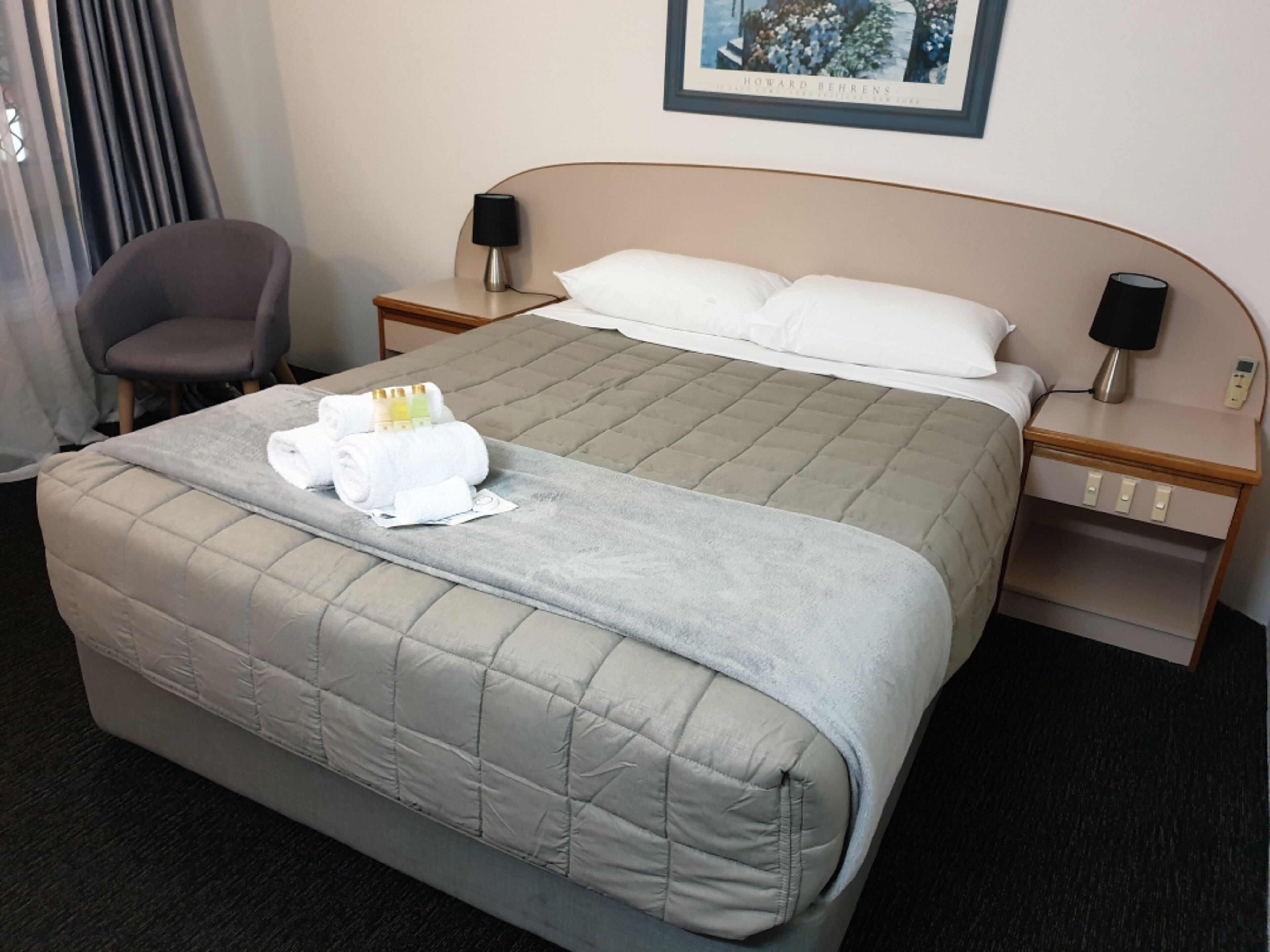A hotel room with a large bed, a chair, two bedside tables with lamps, and a framed picture on the wall.