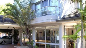Un edificio de dos pisos con fachada de vidrio, un acceso cubierto y un automóvil estacionado adelante.