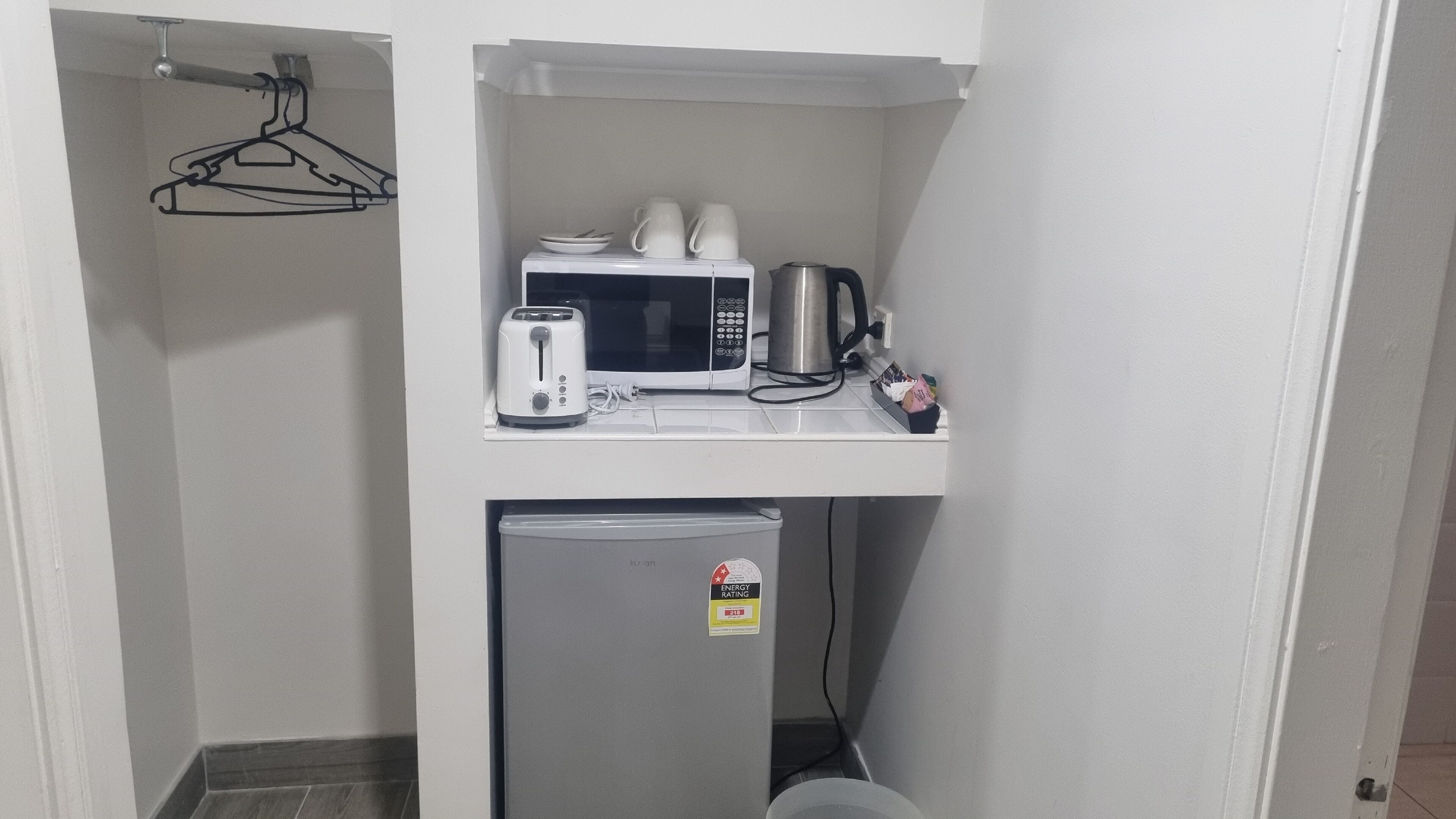 A compact kitchenette with a microwave, toaster, and kettle on a white countertop.