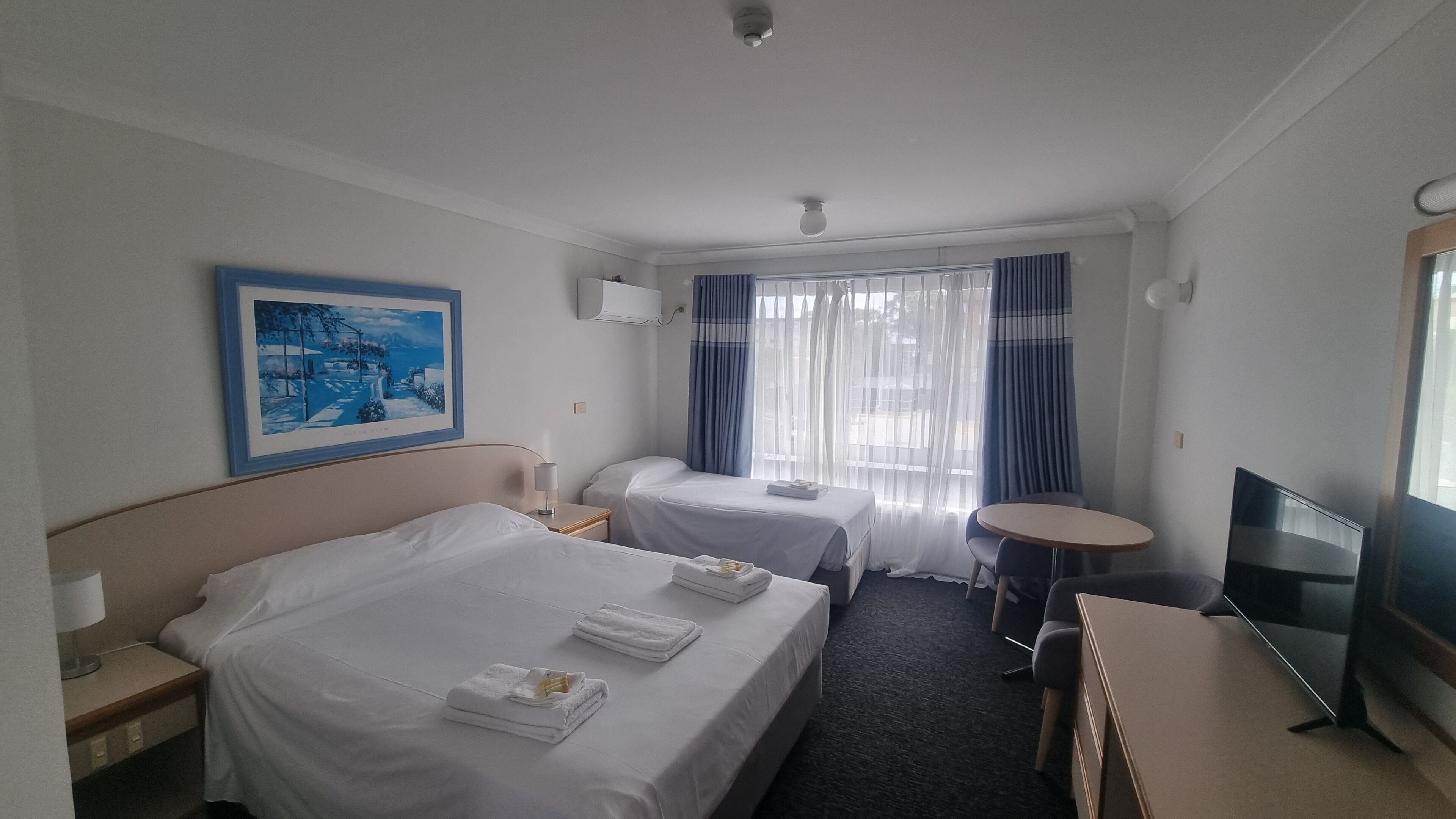 Una habitación de hotel con dos camas, un televisor, una mesita y un cuadro en la pared.