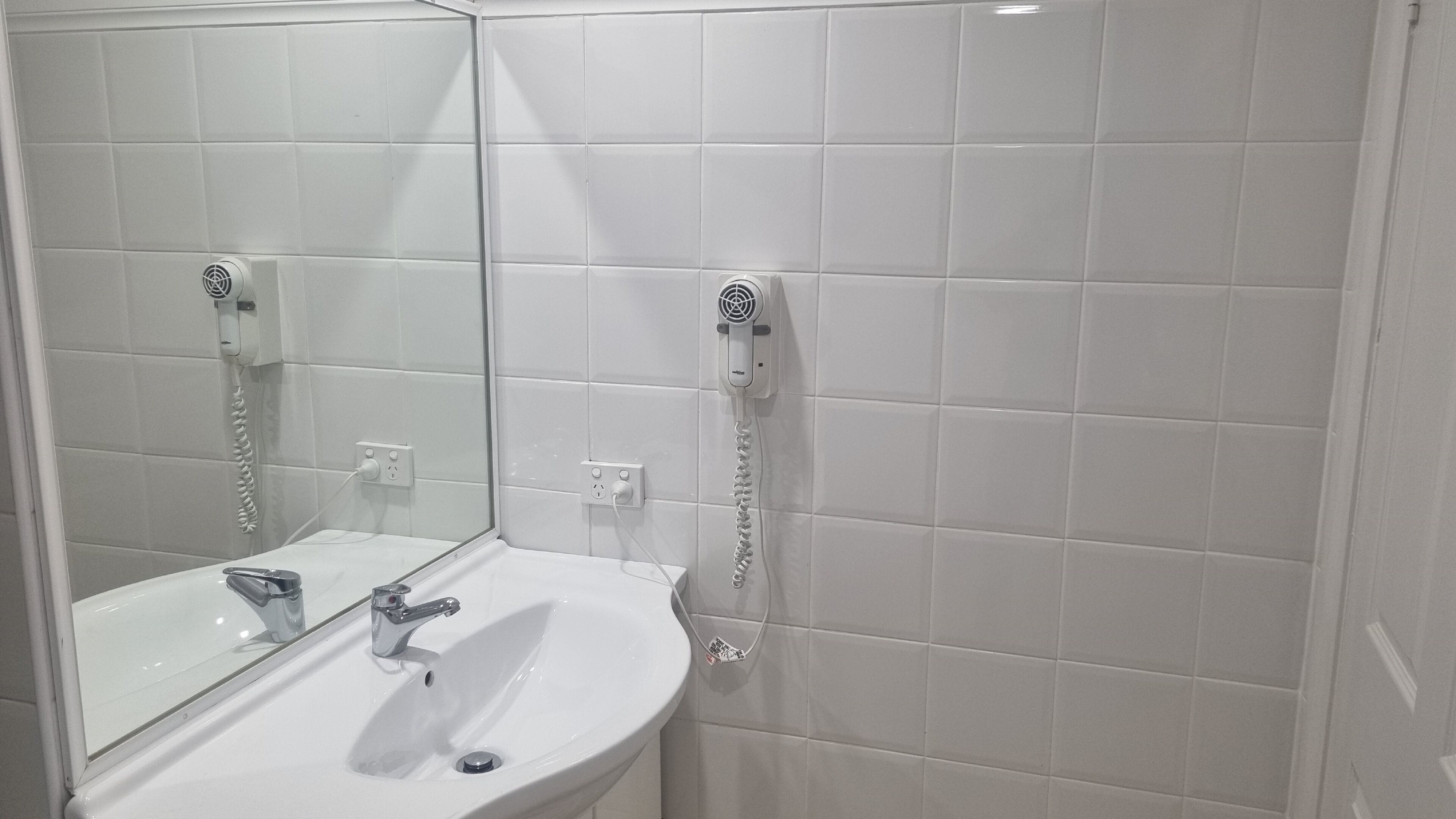 Un baño con un lavamanos blanco, un espejo y un secador de pelo montado en la pared.