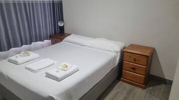 A neatly made bed with white linens and towels, a wooden nightstand with drawers, and a window with curtains.