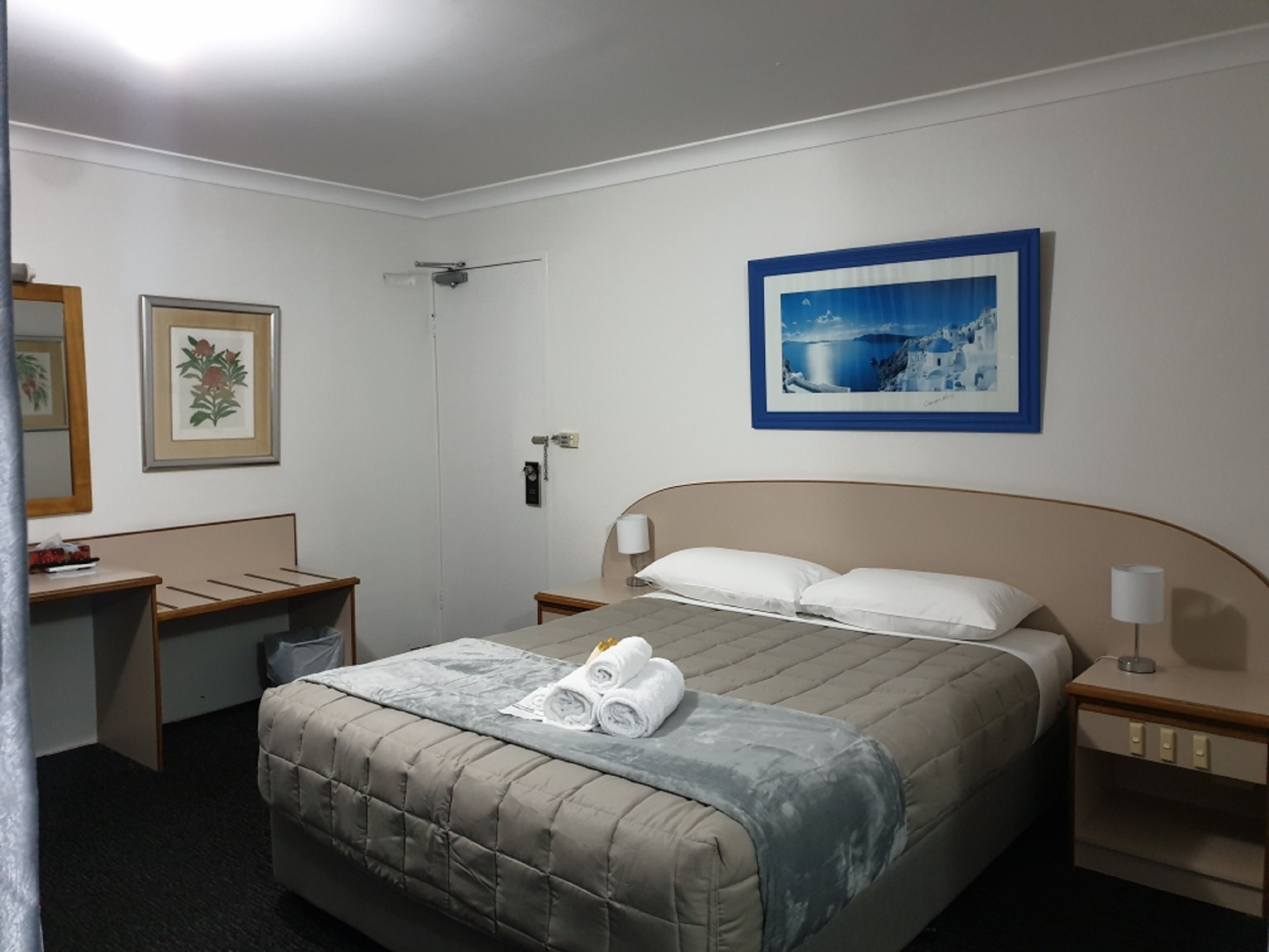 A hotel room with a bed, a desk, a chair, a bathroom, and a framed picture on the wall.
