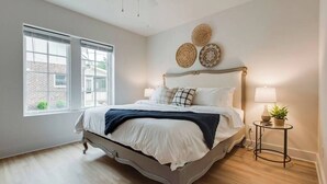 Un dormitorio con cama, dos ventanas, ventilador de techo y decoración en las paredes.