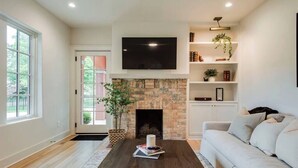 Una sala de estar moderna con chimenea de piedra, un televisor de pantalla plana montado encima, un sofá de color claro y una estantería con objetos decorativos.