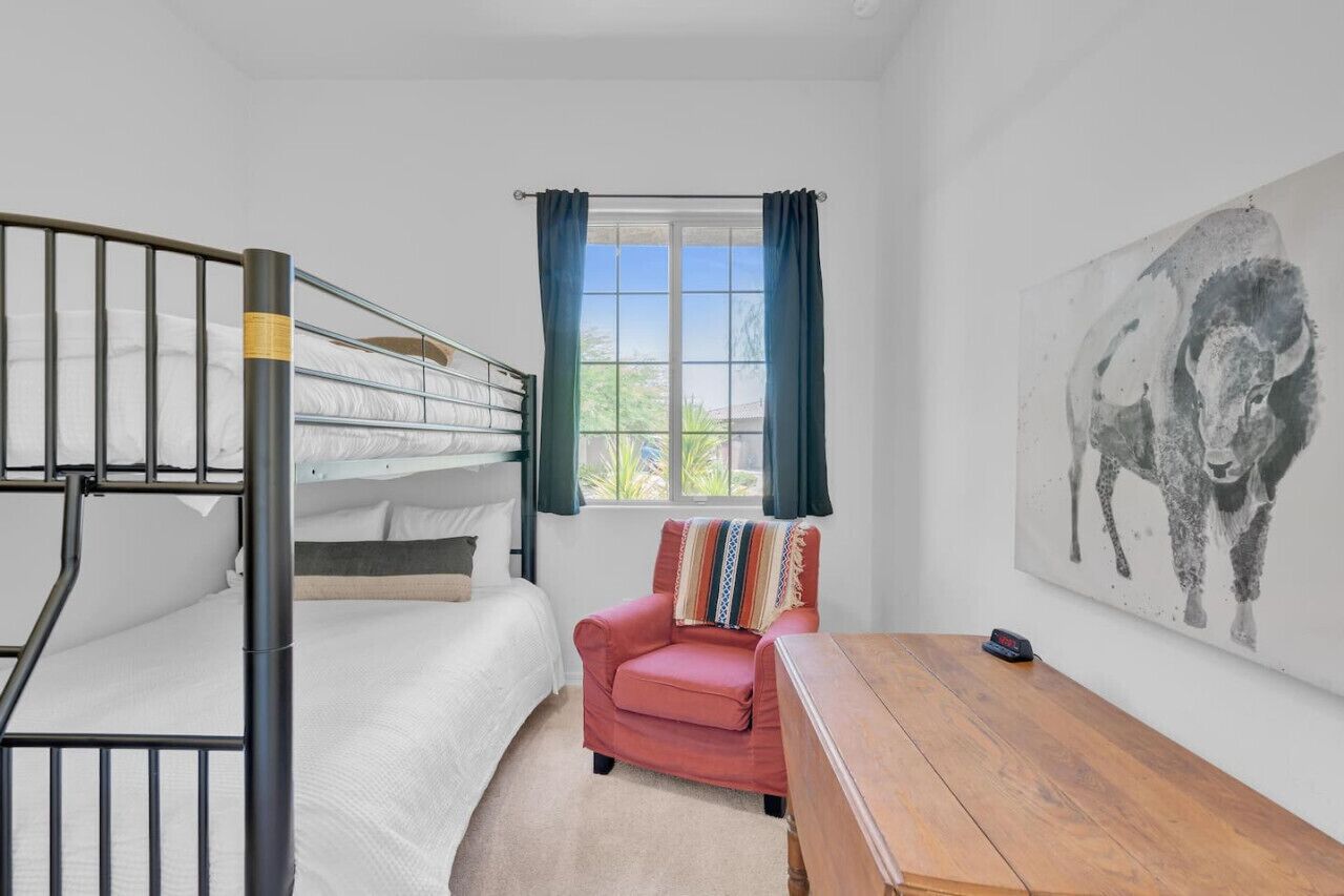 Ein Schlafraum mit Etagenbetten, einem Fenster, einem Stuhl, einem Tisch und einem Bild an der Wand.