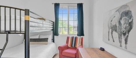 Ein Schlafraum mit Etagenbetten, einem Fenster, einem Stuhl, einem Tisch und einem Bild an der Wand.
