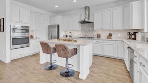 A modern kitchen with white cabinetry, stainless steel appliances, and a central island with bar stools. - Design Dream / View / 4 BR 3 BA / Upscale / Garage (Sahuarita)