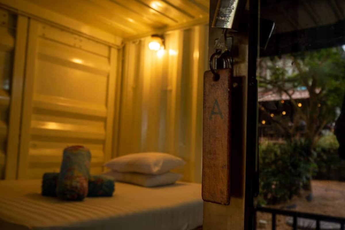 A bed with a pillow and a blanket, a small table with a bottle, and a sign with the letter 'A' on a wooden post.