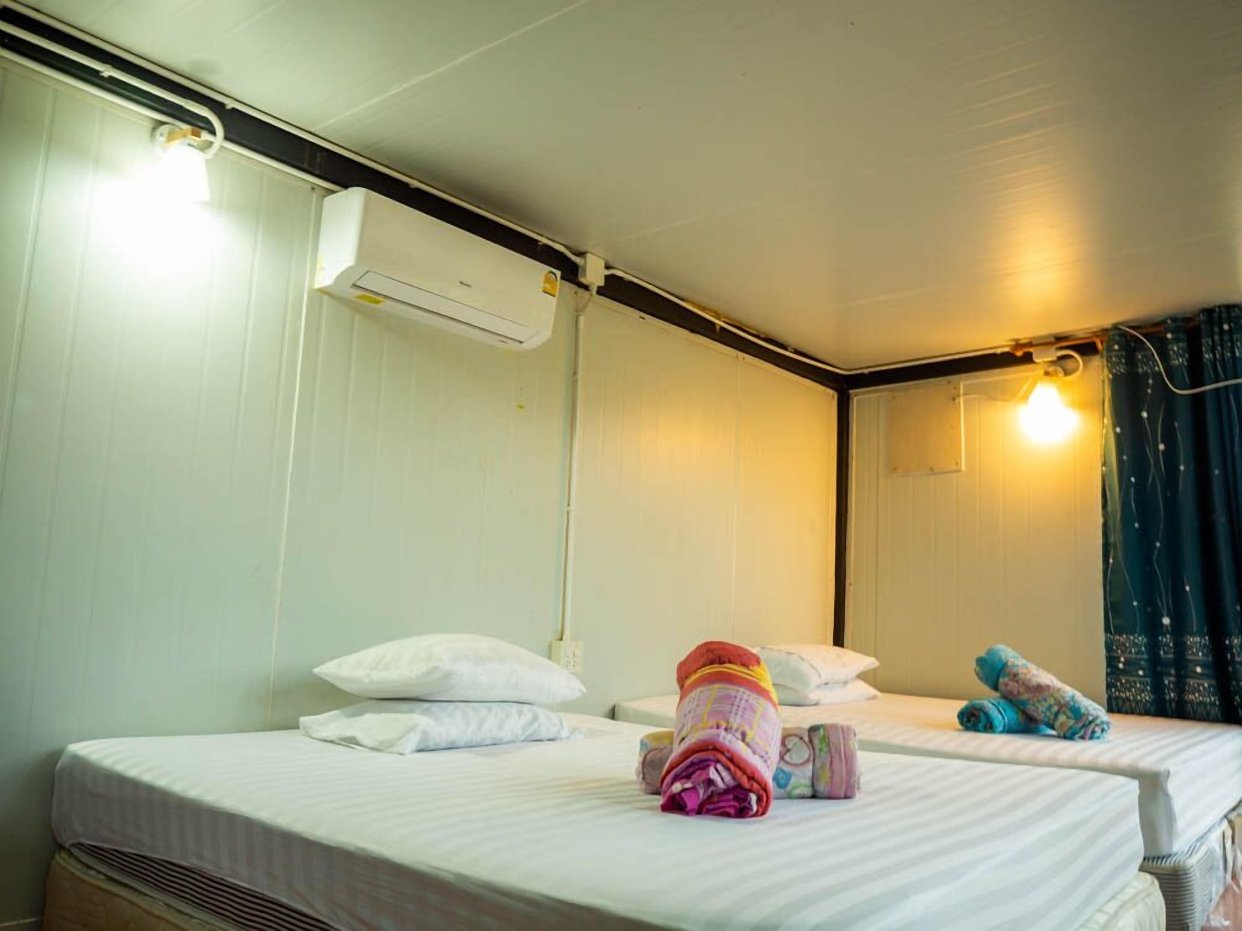 A hotel room with two beds, white bedding, a wall-mounted air conditioner, and a single light fixture.