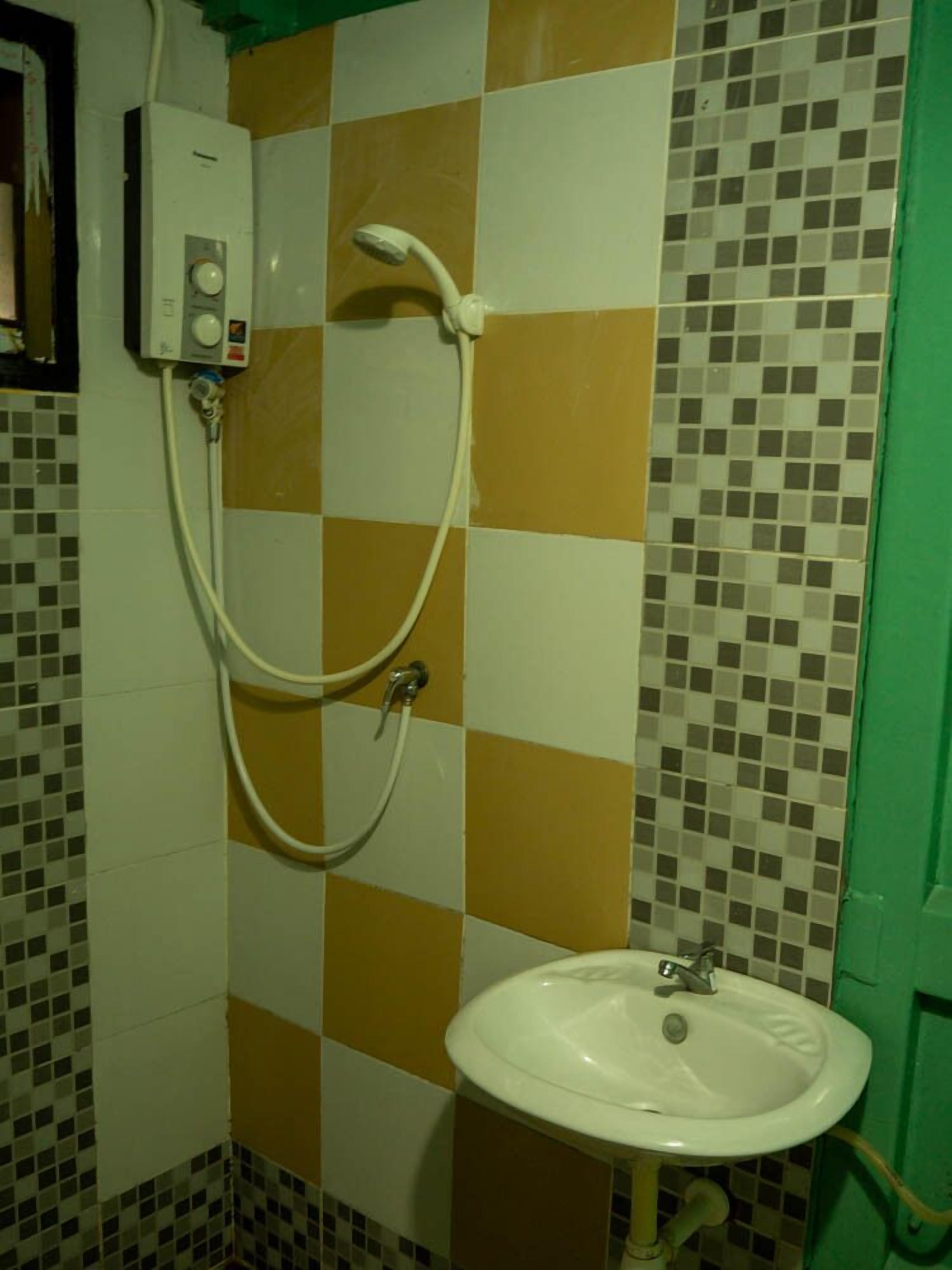 Ein Badezimmer mit gefliestem Boden, einem weißen Waschbecken und einer Dusche mit Duschbrause.