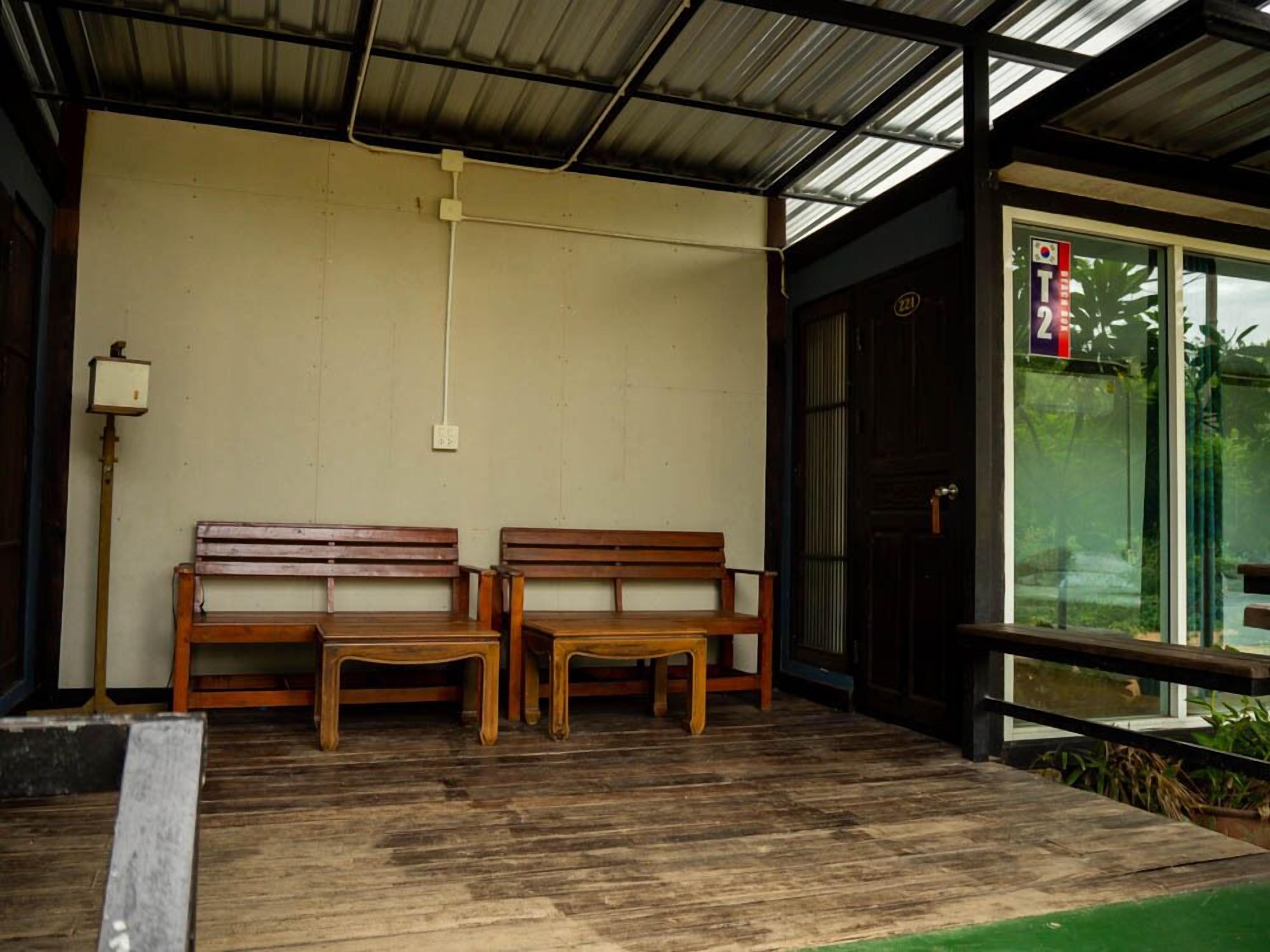 Un espacio al aire libre cubierto con dos bancos de madera y una mesa, un accesorio de iluminación en la pared y una puerta con un cartel.