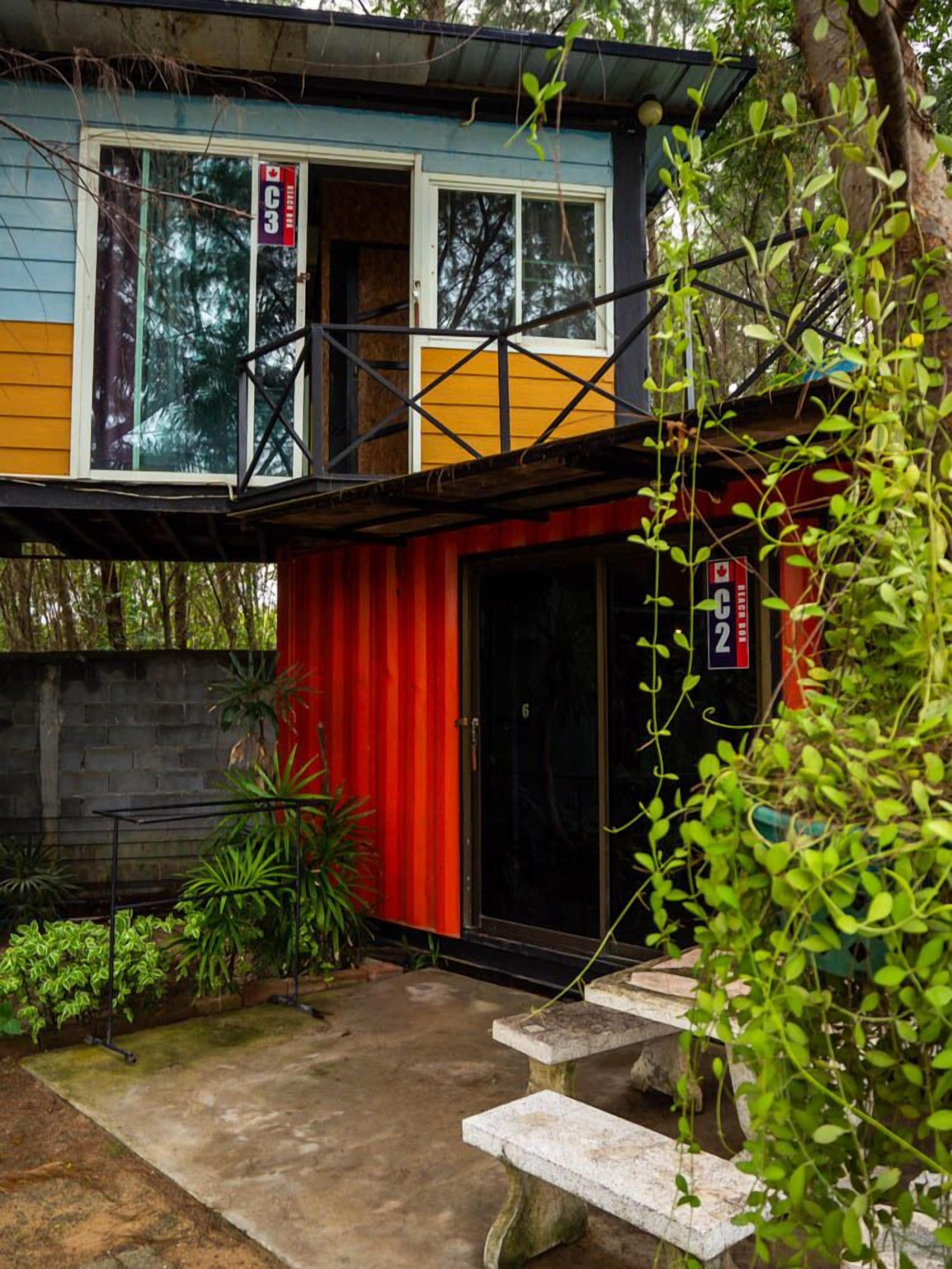 A two-story house with a red and yellow exterior, a black door, and a small balcony.