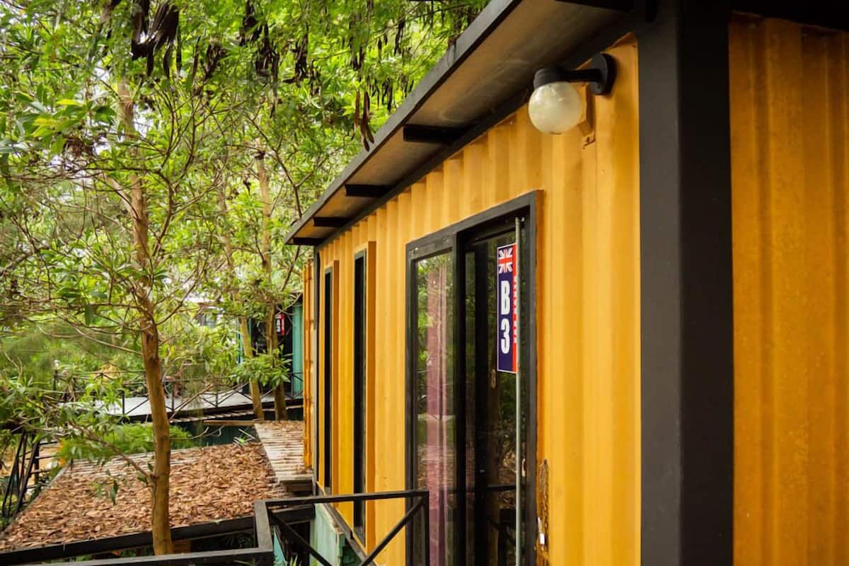 A yellow building with a black door, surrounded by trees and a wooden deck.