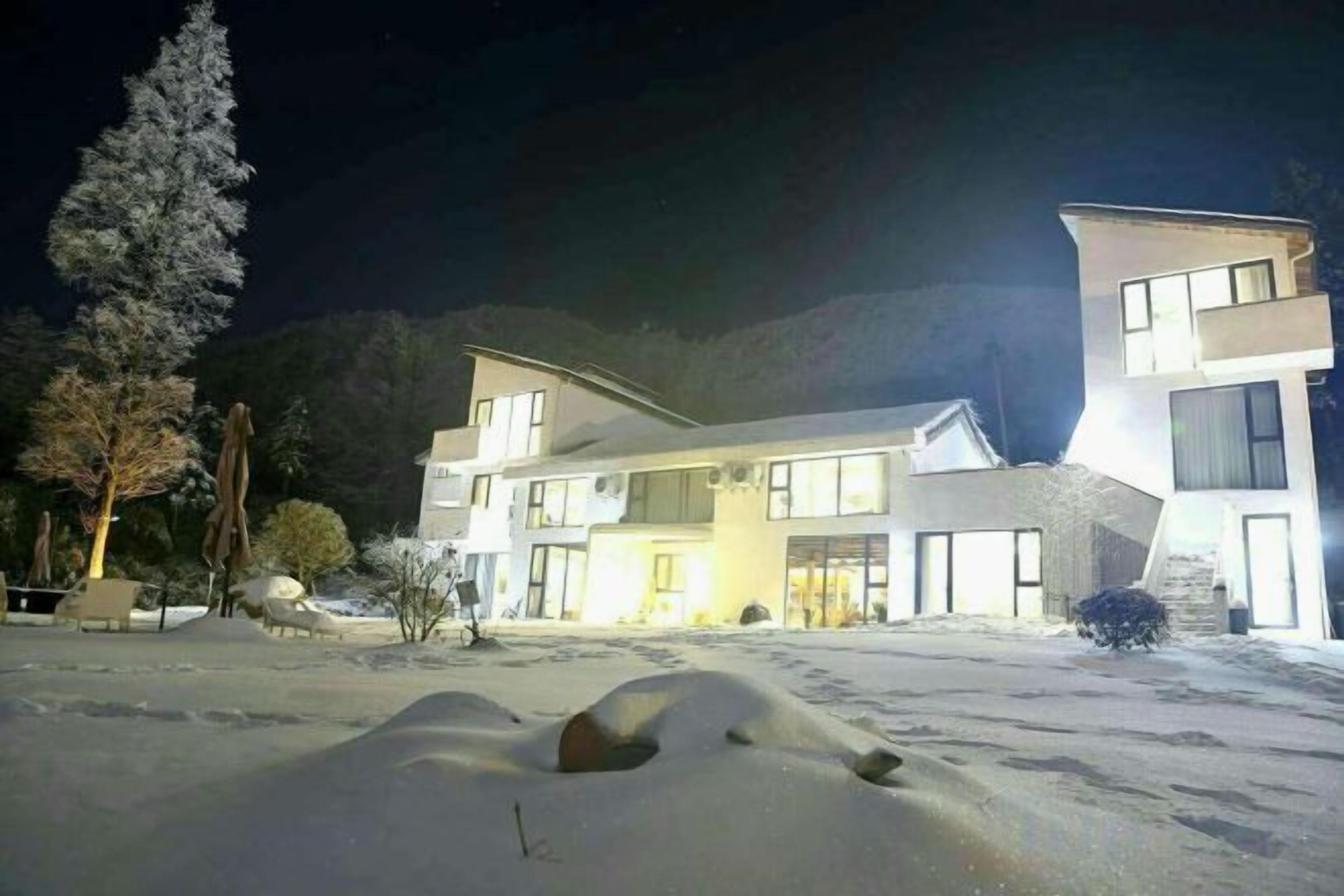 A modern building with a flat roof and large windows, surrounded by snow-covered ground and trees.