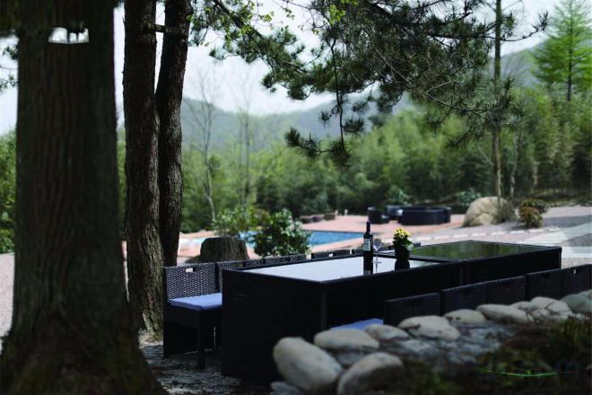 An outdoor seating area with tables and chairs, surrounded by trees and a view of a mountain range.