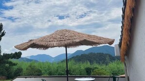 Una habitación con un toldo de paja, vistas a colinas verdes y una cordillera al fondo.