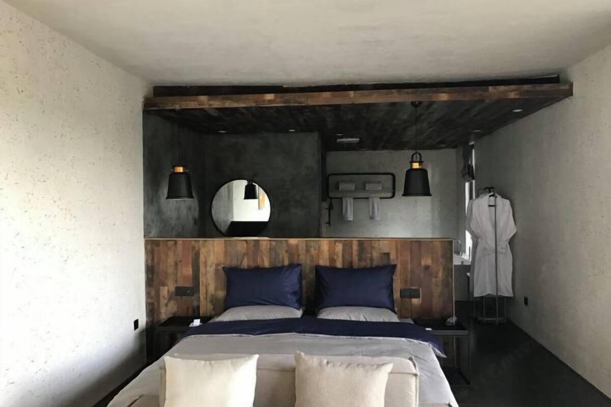 Une chambre à coucher avec une tête de lit en bois, deux lits, des lampes de chevet, un miroir et un peignoir suspendu à un porte-manteau.