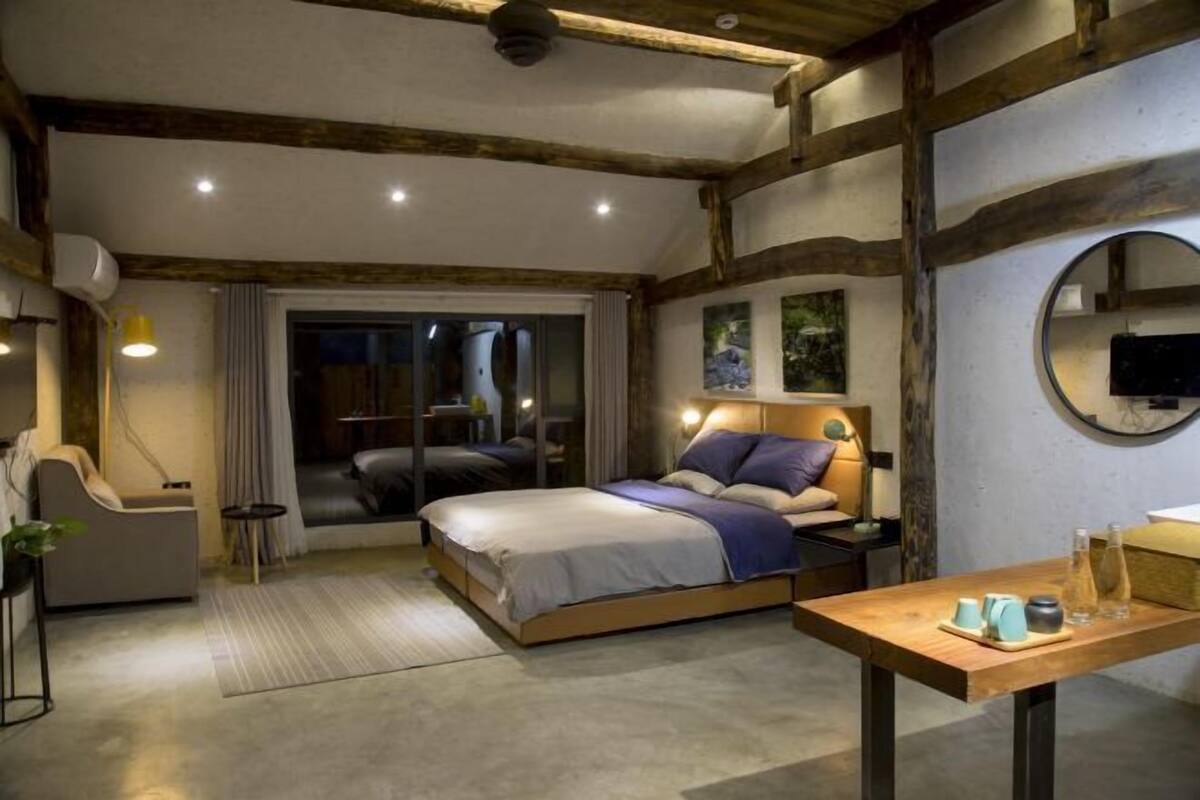 Une chambre à coucher moderne avec un grand lit, des tables de chevet, une tête de lit en bois et une vue sur l’extérieur.