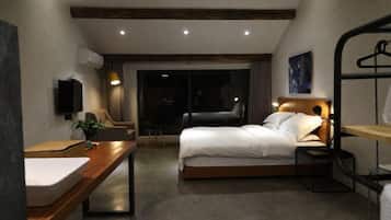 A modern hotel room with a bed, bedside table, and a desk with a chair.
