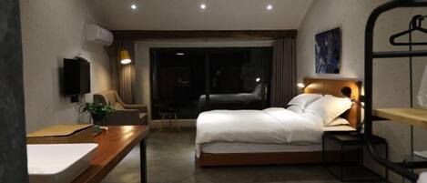 A modern hotel room with a bed, bedside table, and a desk with a chair.