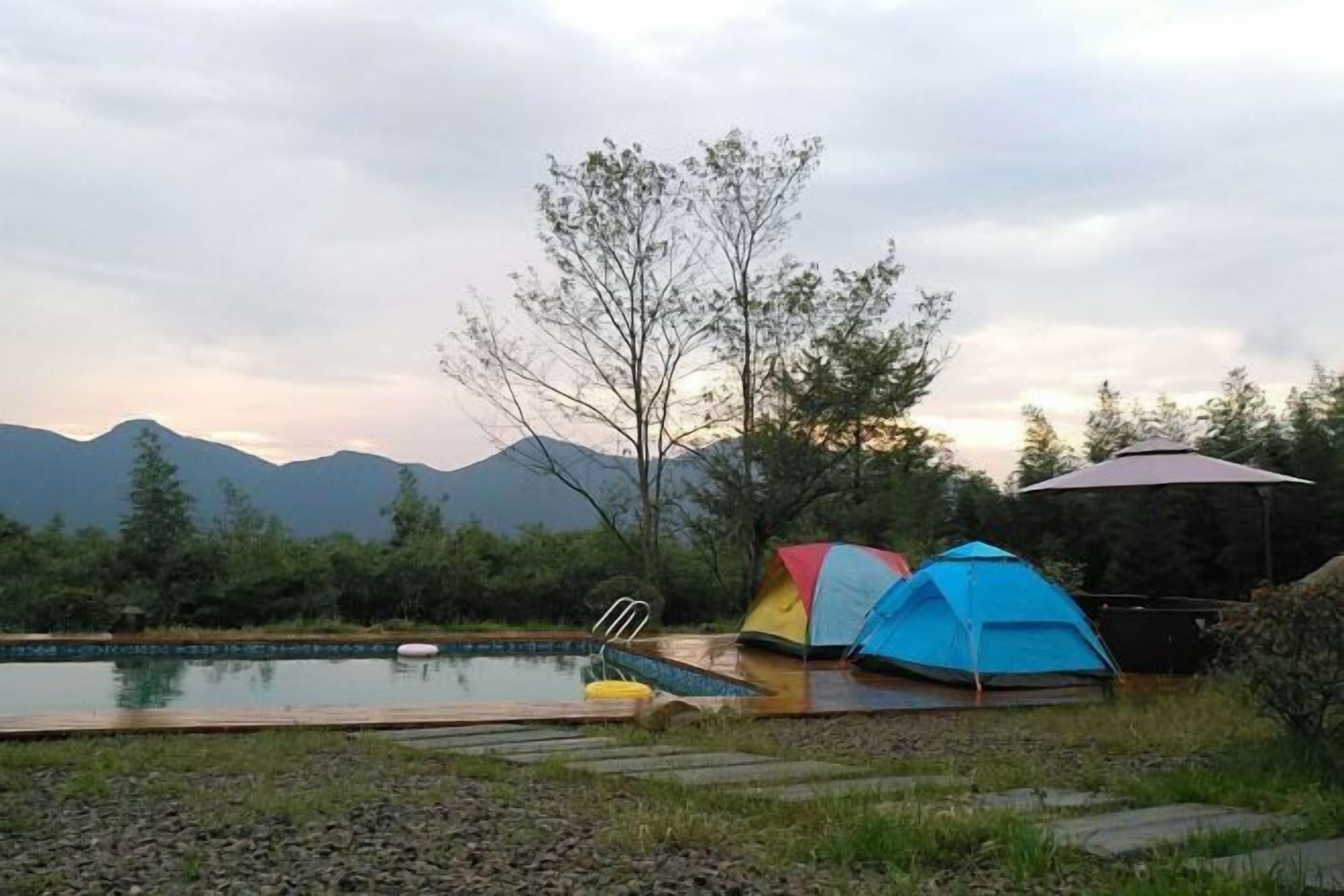 Zona de camping con piscina, tiendas de campaña y vistas a montañas.
