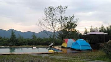 Zona de camping con piscina, tiendas de campaña y vistas a montañas.