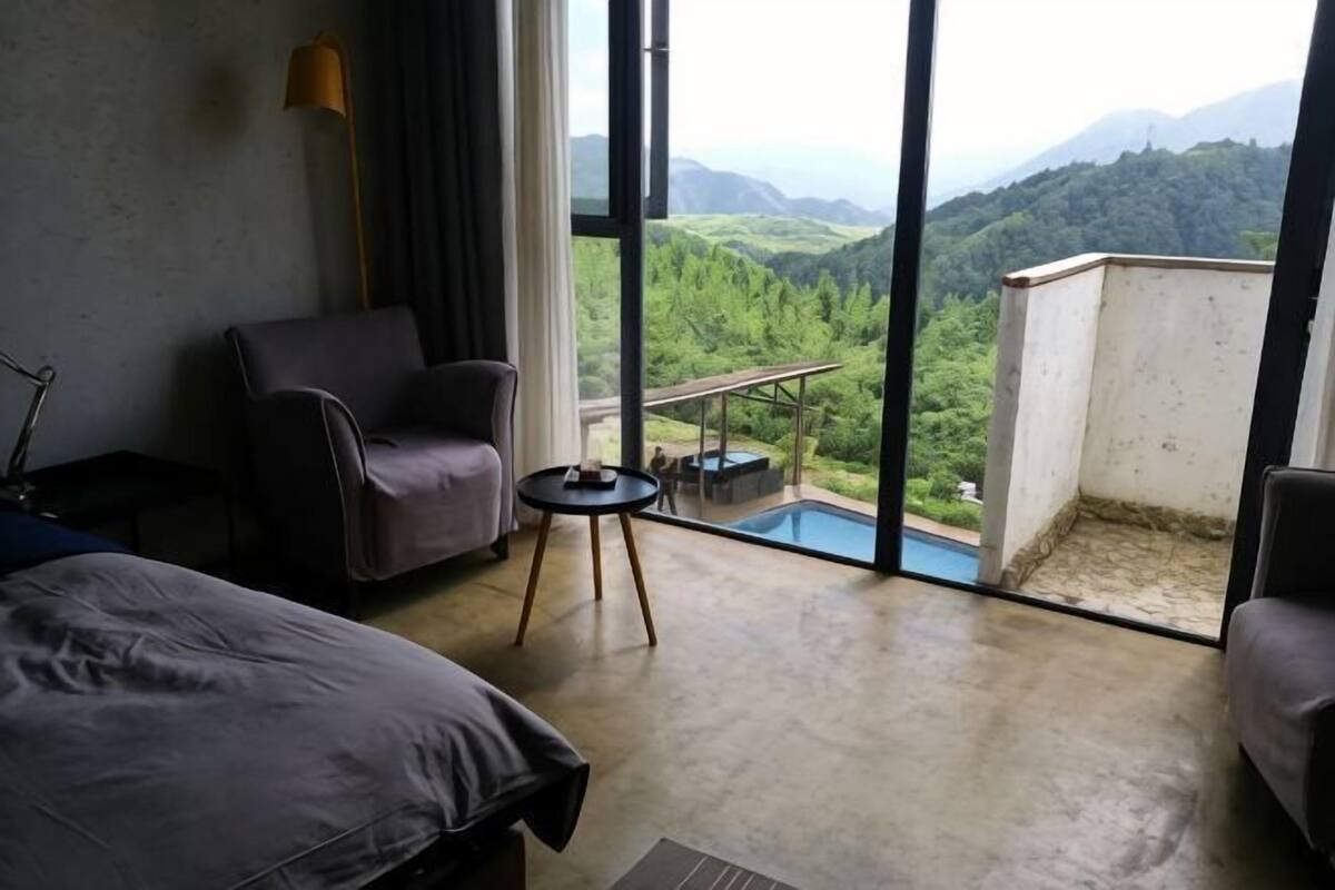 Une chambre avec un lit, une chaise, une petite table et un balcon offrant une vue sur une montagne et la verdure.