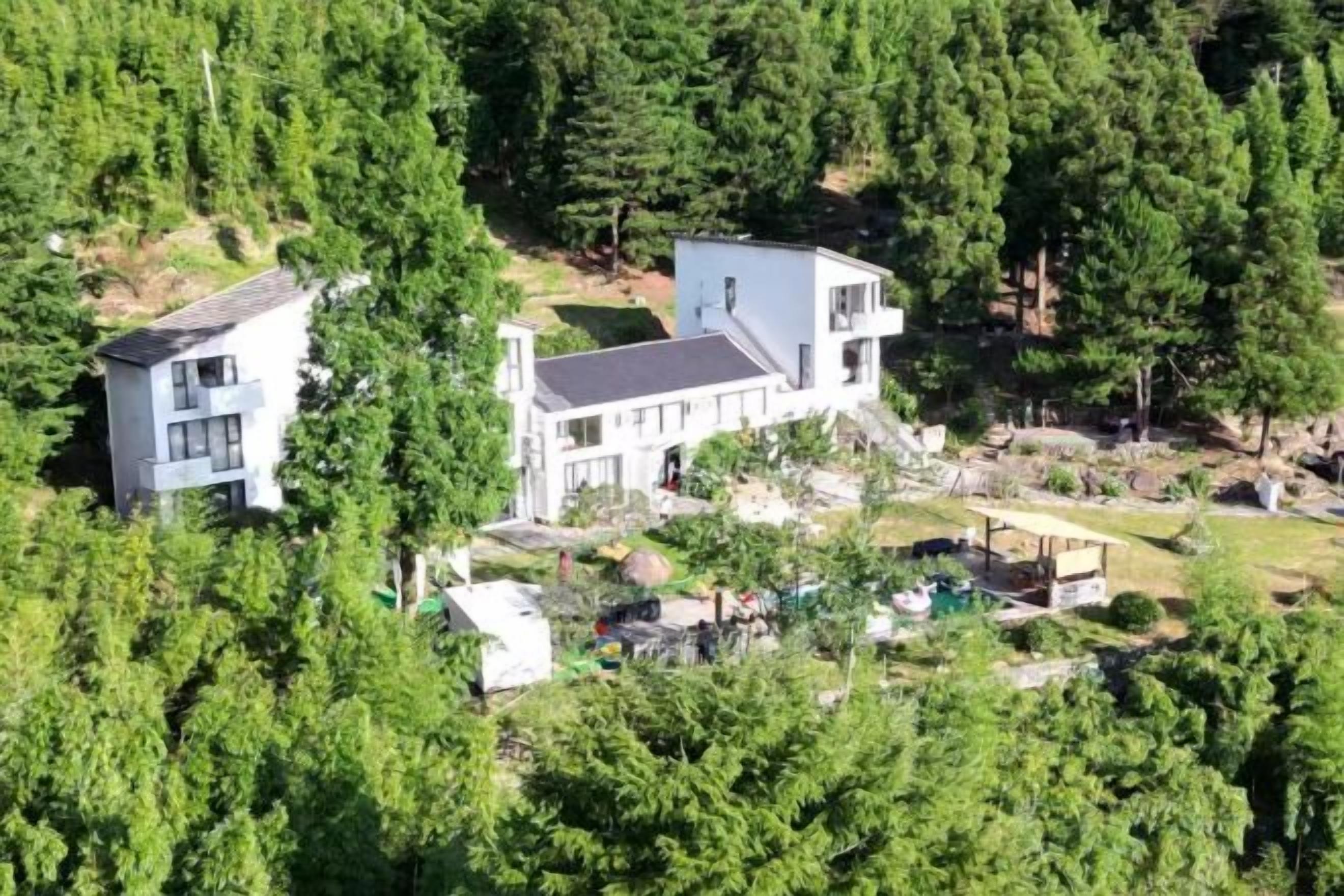 A large, modern two-story house surrounded by dense forest.