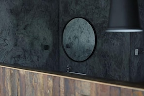 Une salle de bain avec un miroir rond, un comptoir en bois et un mur orné d’un motif texturé.