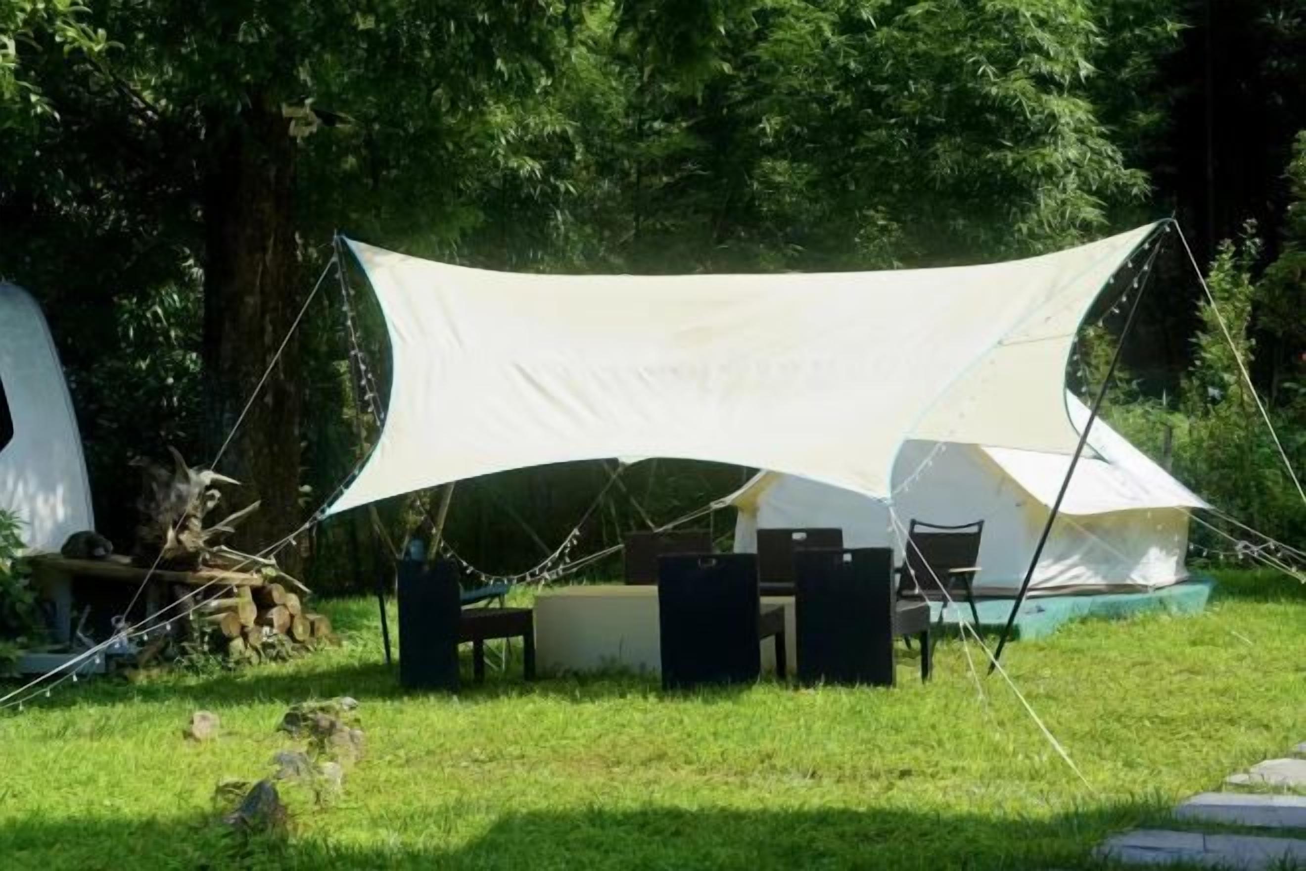 Un campamento equipado con un toldo grande, una mesa, sillas y un altavoz.
