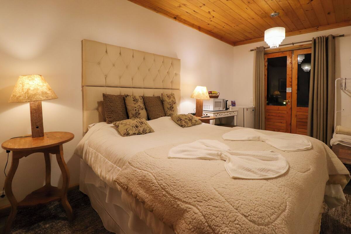 A bedroom with a large bed, two bedside lamps, a wooden headboard, and a wooden door with curtains.