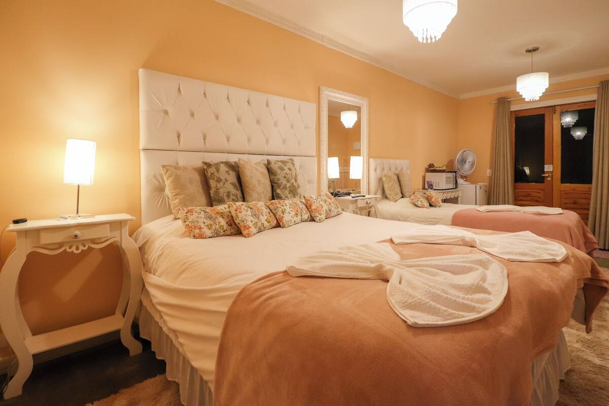A hotel room with two beds, a large mirror, a bedside table with a lamp, and a fan.
