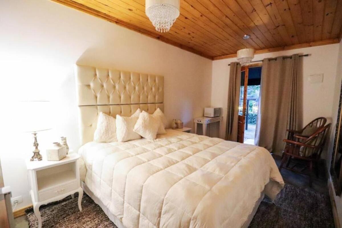 A bedroom with a large bed, a nightstand, a wooden ceiling, and a chandelier.