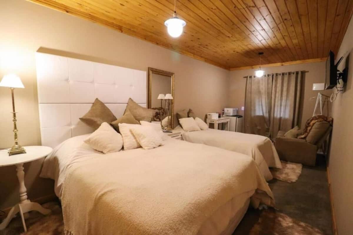 A bedroom with two beds, a wooden ceiling, a bedside table, a chair, and a mirror.