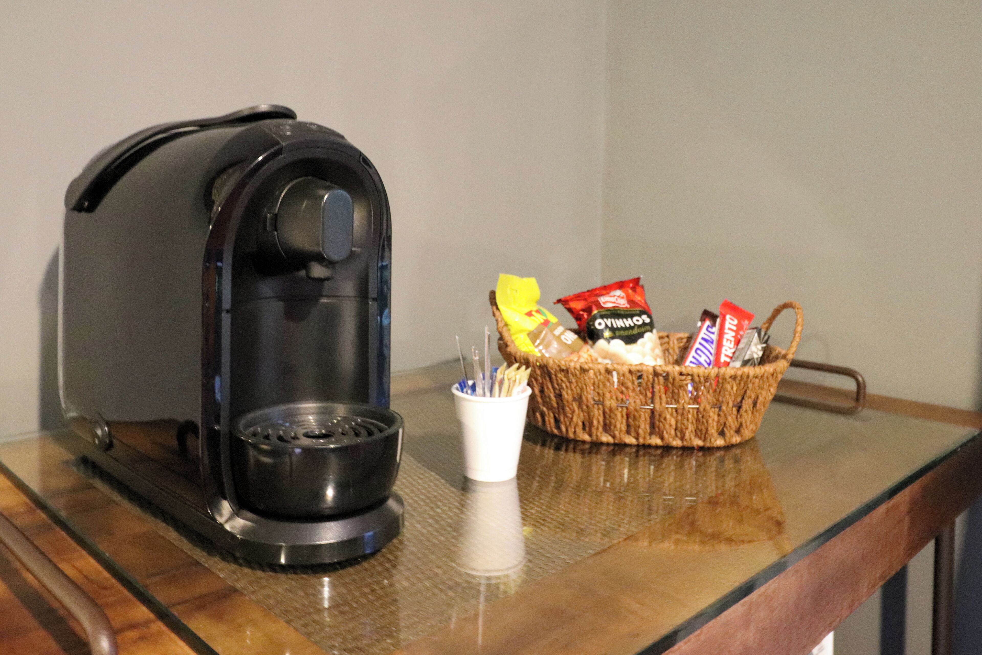 A coffee maker, a basket with snacks, and a cup on a wooden table.