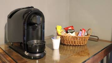 A coffee maker, a basket with snacks, and a cup on a wooden table.